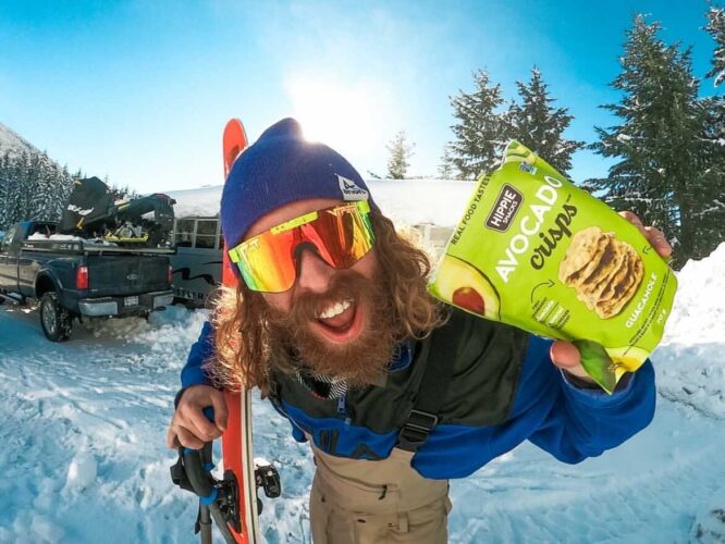 Man holding Hippie Snacks up to the camera with his skis and pit viper sunglasses